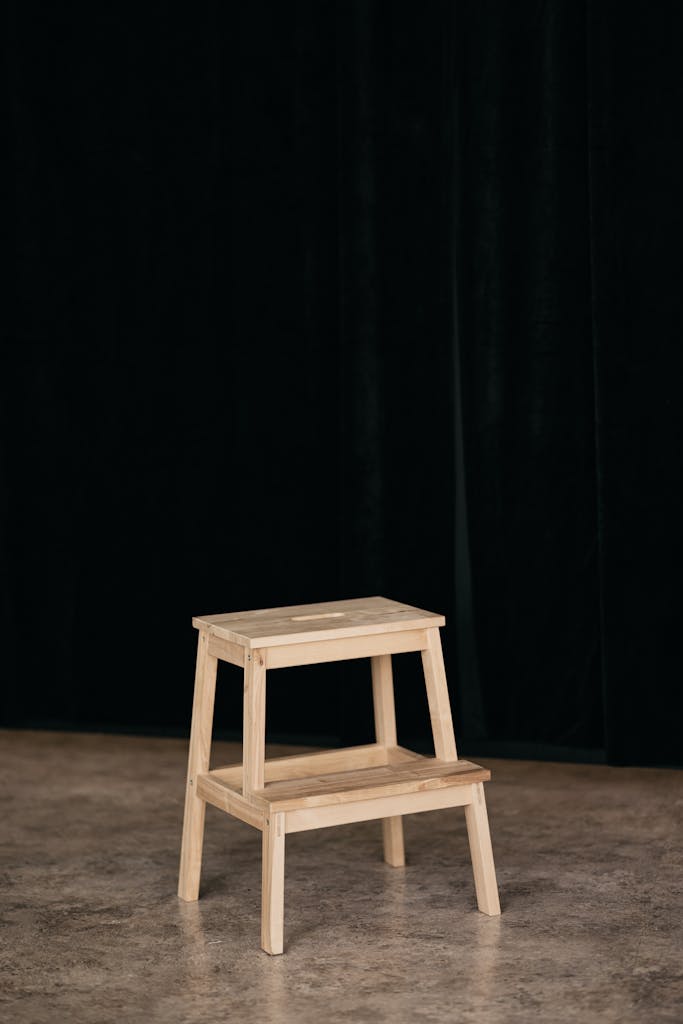 17 Easy Woodworking Projects for Beginners (Simple & Fun!) 10 A simple wooden step stool in front of a black curtain on a stone floor.
